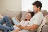 side view of a relaxed young couple reading book on couch at hom